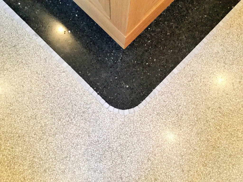 Eckdetail heller Terrazzo mit schwarzem Fries und Wandvertäfelung aus Holz